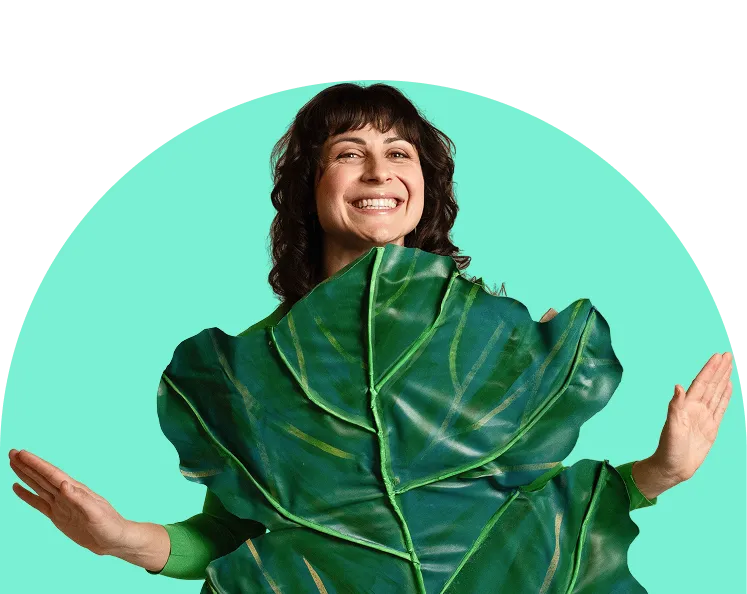 A person with long hair wearing glasses is sitting at a desk, looking at a laptop screen, and biting a yellow pencil in frustration. There is a cup filled with colored pencils in the foreground.